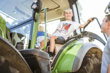 Kind auf dem Traktor - mithilfe bei der Stallarbeit auf dem Bauernhof